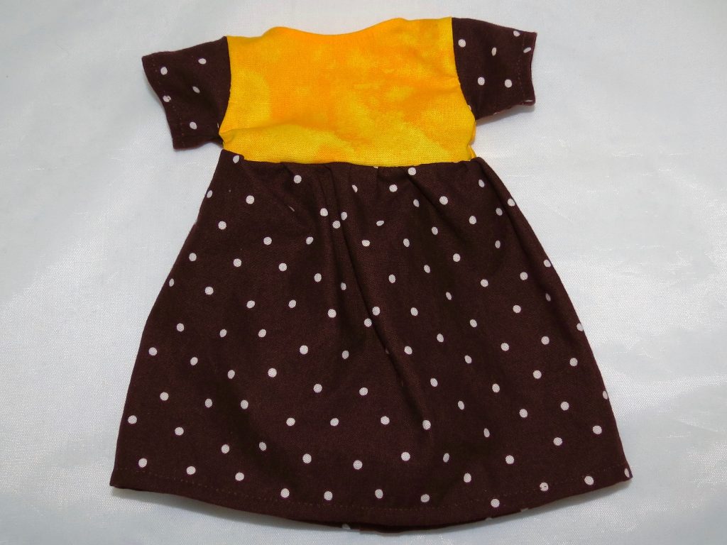A brown doll dress with small white polka dots and a yellow bodice.